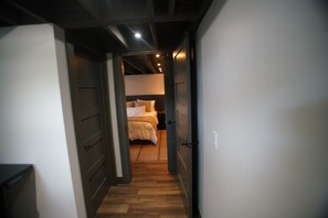 A narrow hallway leading to a bedroom with a bed and nightstands. - Black, White, & Barn w/ Hot Tub & Fire Pit (Fredericktown)