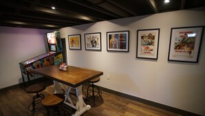 Una habitació amb una taula de fusta i tamborets de bar, cartells de pel·lícules emmarcats a la paret i un jukebox.