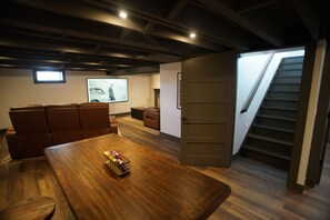 A conference room with a wooden table, brown leather chairs, a projector screen, and a staircase leading to an upper level.