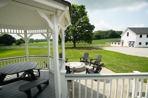 A covered outdoor seating area with picnic tables and chairs, overlooking a grassy field and a white barn. - Black, White, & Barn w/ Hot Tub & Fire Pit (Fredericktown)