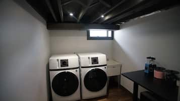 A laundry room with two front-loading washing machines, a small window, and a table with cleaning supplies.