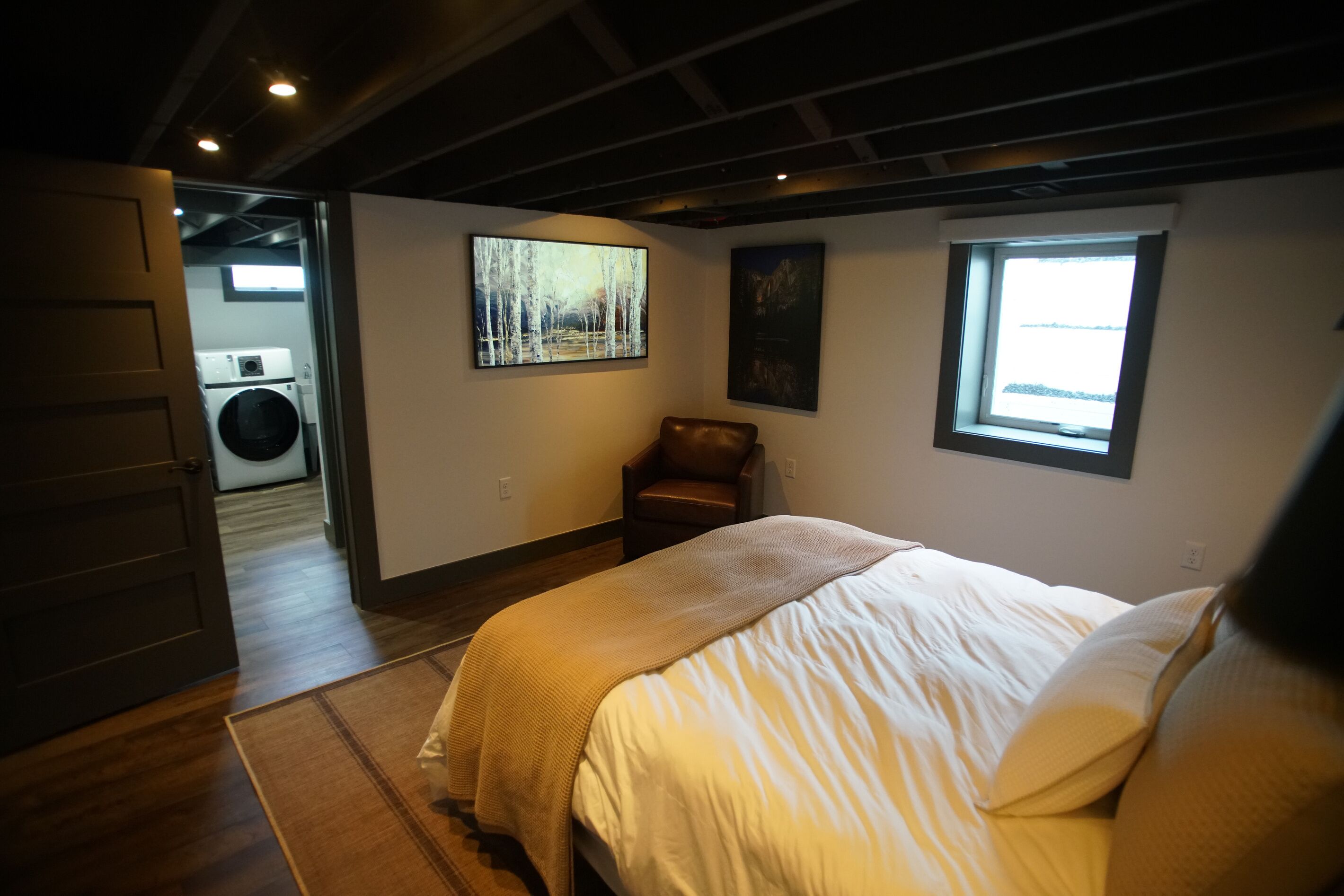 A bedroom with a bed, a chair, a painting, and a window.