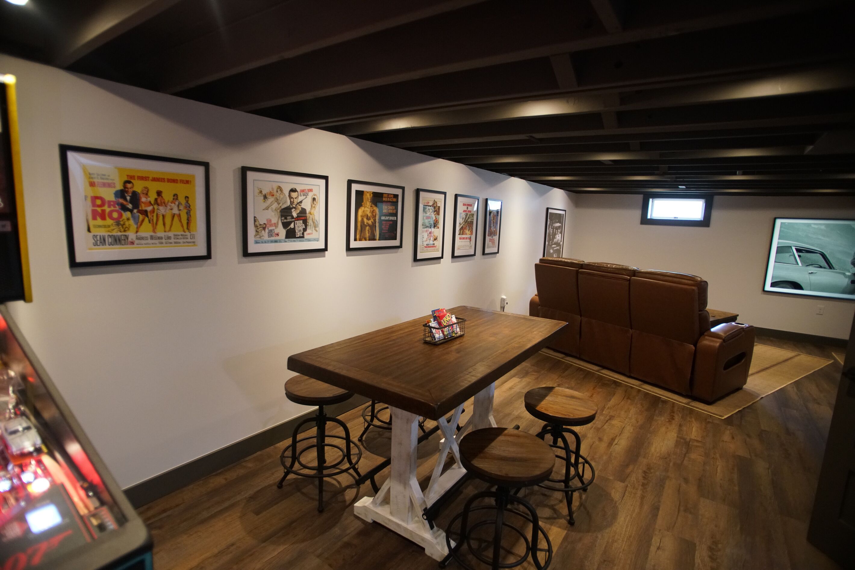A room with a wooden table, stools, a cushioned bench, and framed movie posters on the wall.