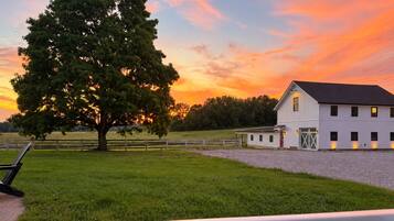 A barn with a large tree in the foreground, a fenced area, and a clear sky.