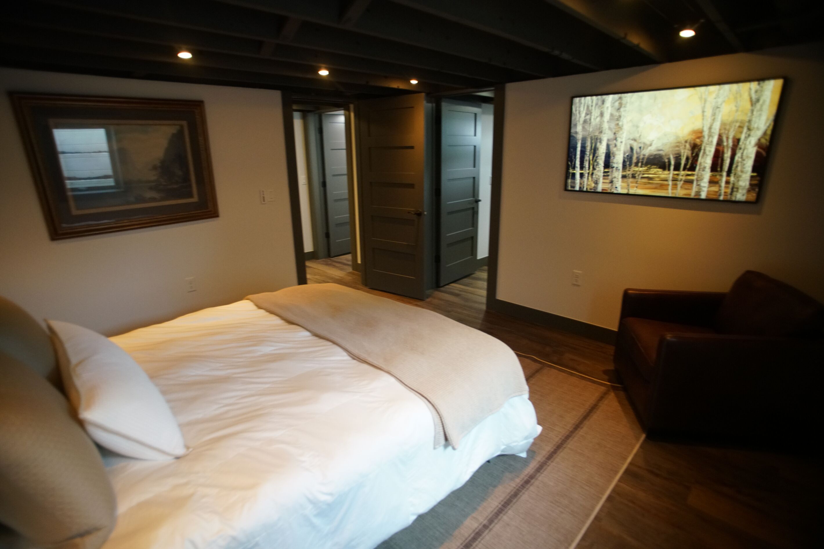A bedroom with a bed, a chair, a painting, and a door leading to another room.