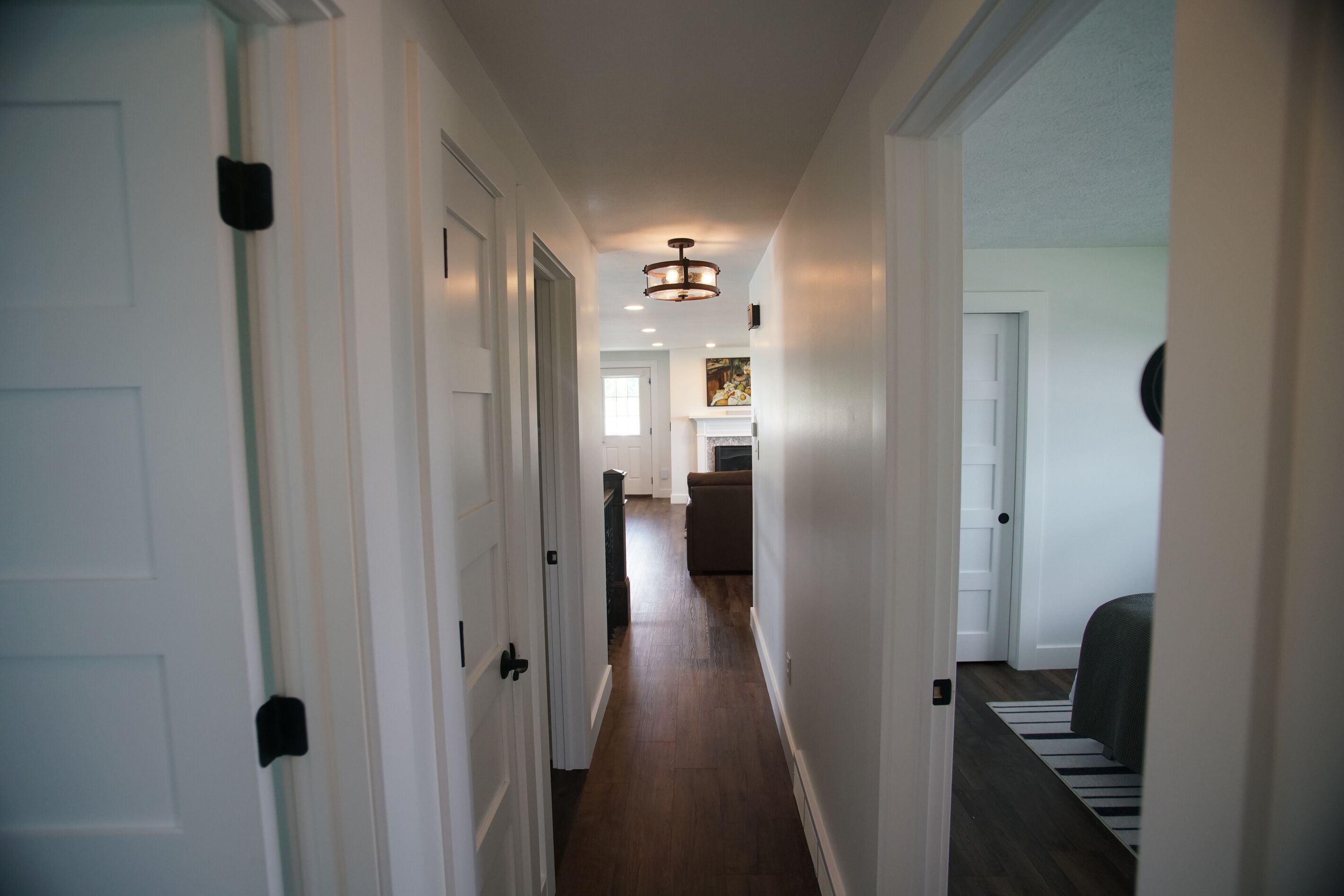 A hallway with white doors, a wooden floor, and a ceiling light fixture.
