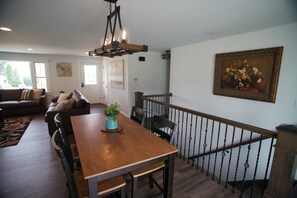 A dining area with a wooden table and chairs, a staircase with a railing, and a painting on the wall. - Black, White, & Barn w/ Hot Tub & Fire Pit (Fredericktown)