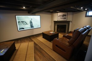 A living room with a large screen, a fireplace, leather recliner, and a coffee table.