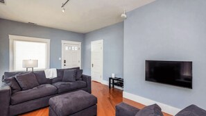A living room with a grey sofa, a flat-screen TV mounted on the wall, and a lamp on a side table. - Bungalow on Vine by Avantstay Walkable Downtown + Private Yard Paso Robles Wine Country (Paso Robles)
