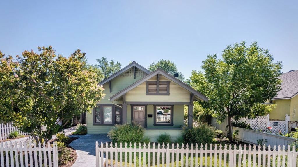 A two-story house with a front porch, a picket fence, and a well-maintained lawn.