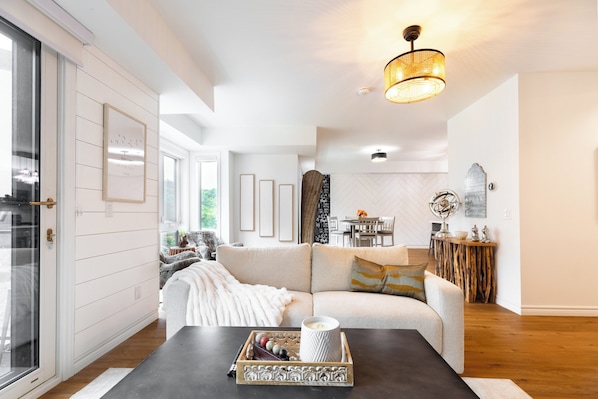 A modern living room with a sofa, a coffee table, and a dining area in the background.