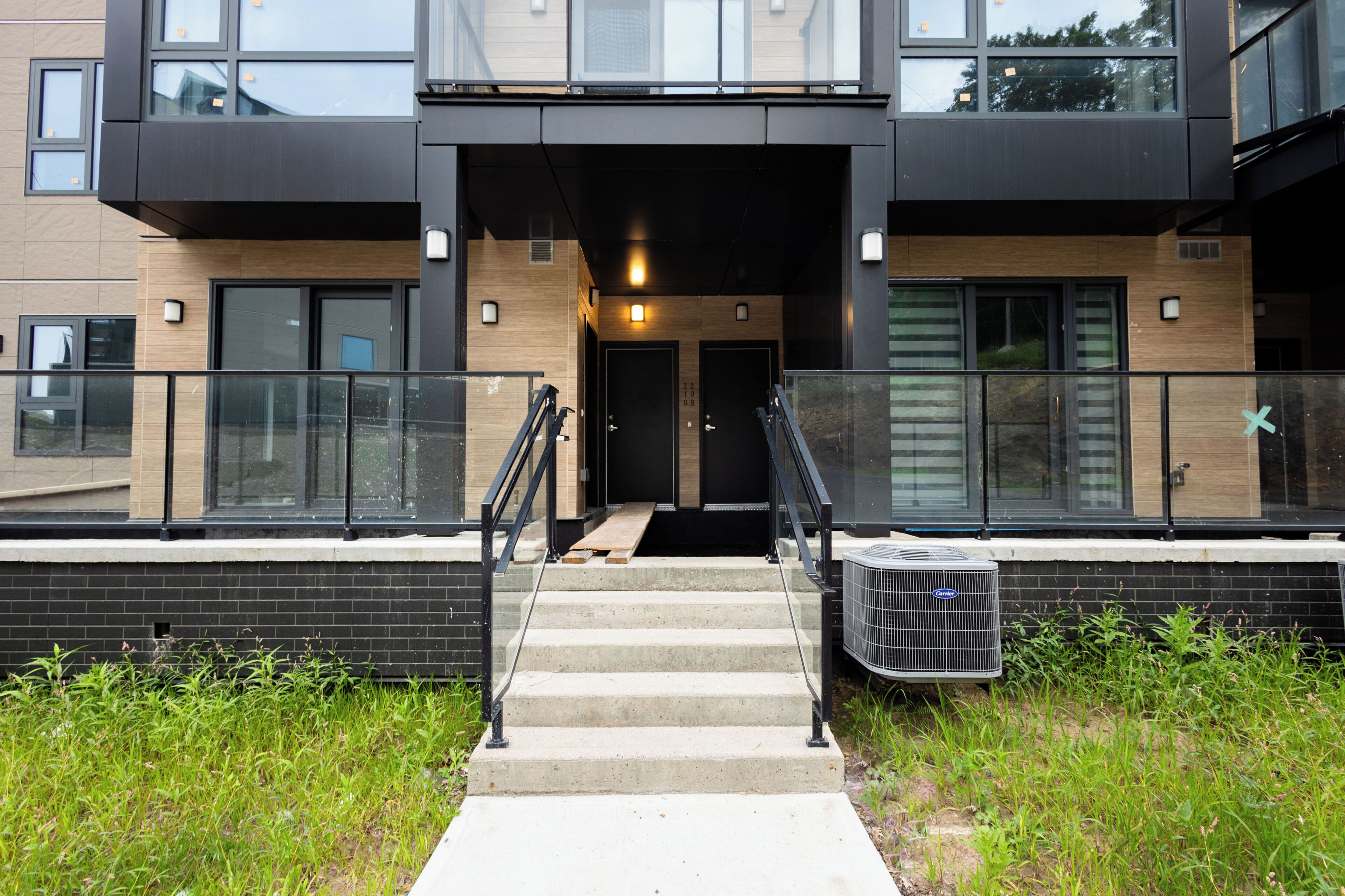 A modern building with a staircase leading to a door, a small outdoor area with steps, and a large air conditioning unit.