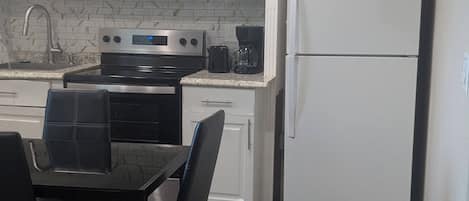 A kitchen with white cabinets, a double refrigerator, a microwave, and a dining area with a table and chairs.
