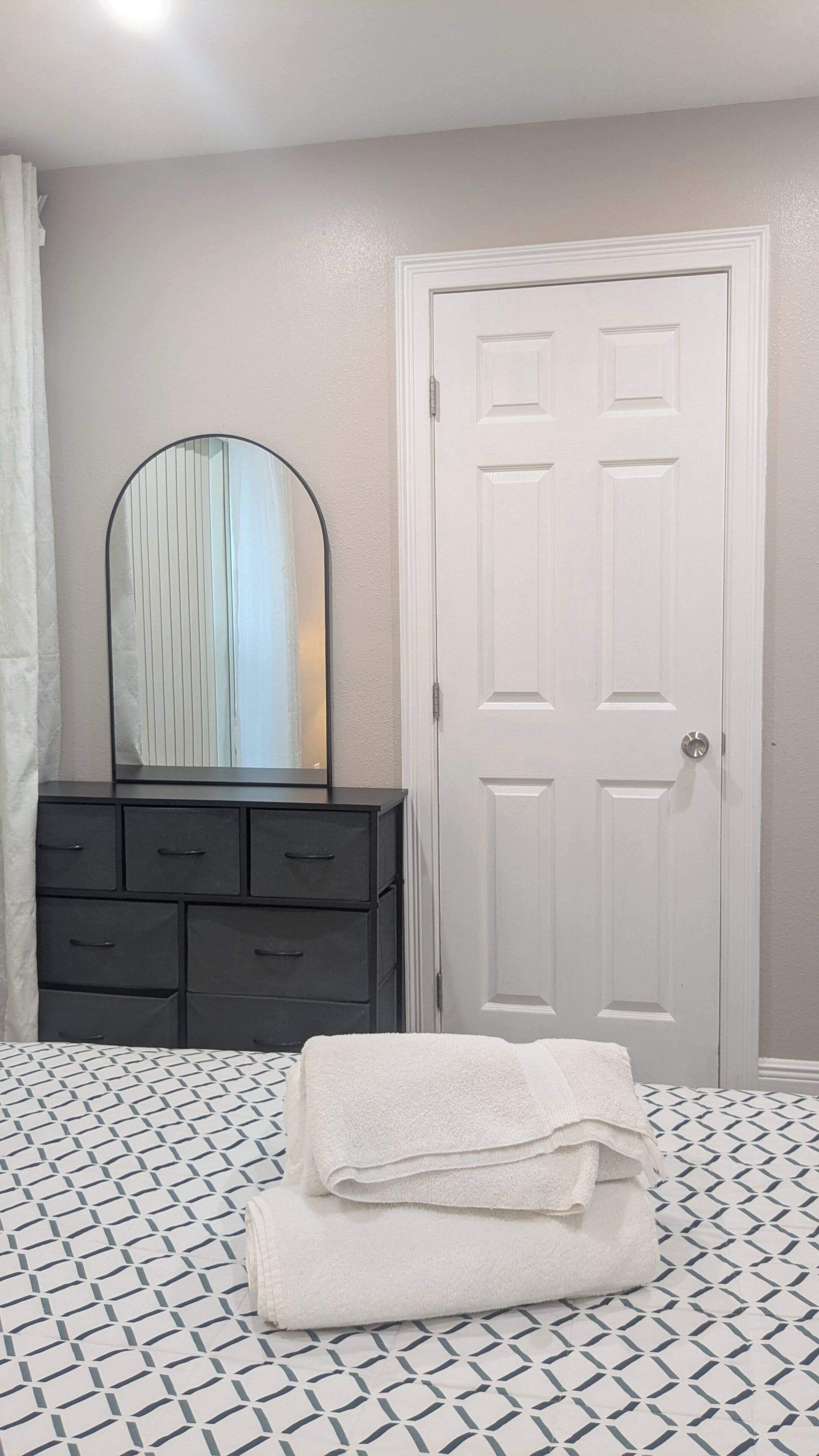 Un dormitorio con cama, cómoda, espejo y puerta.