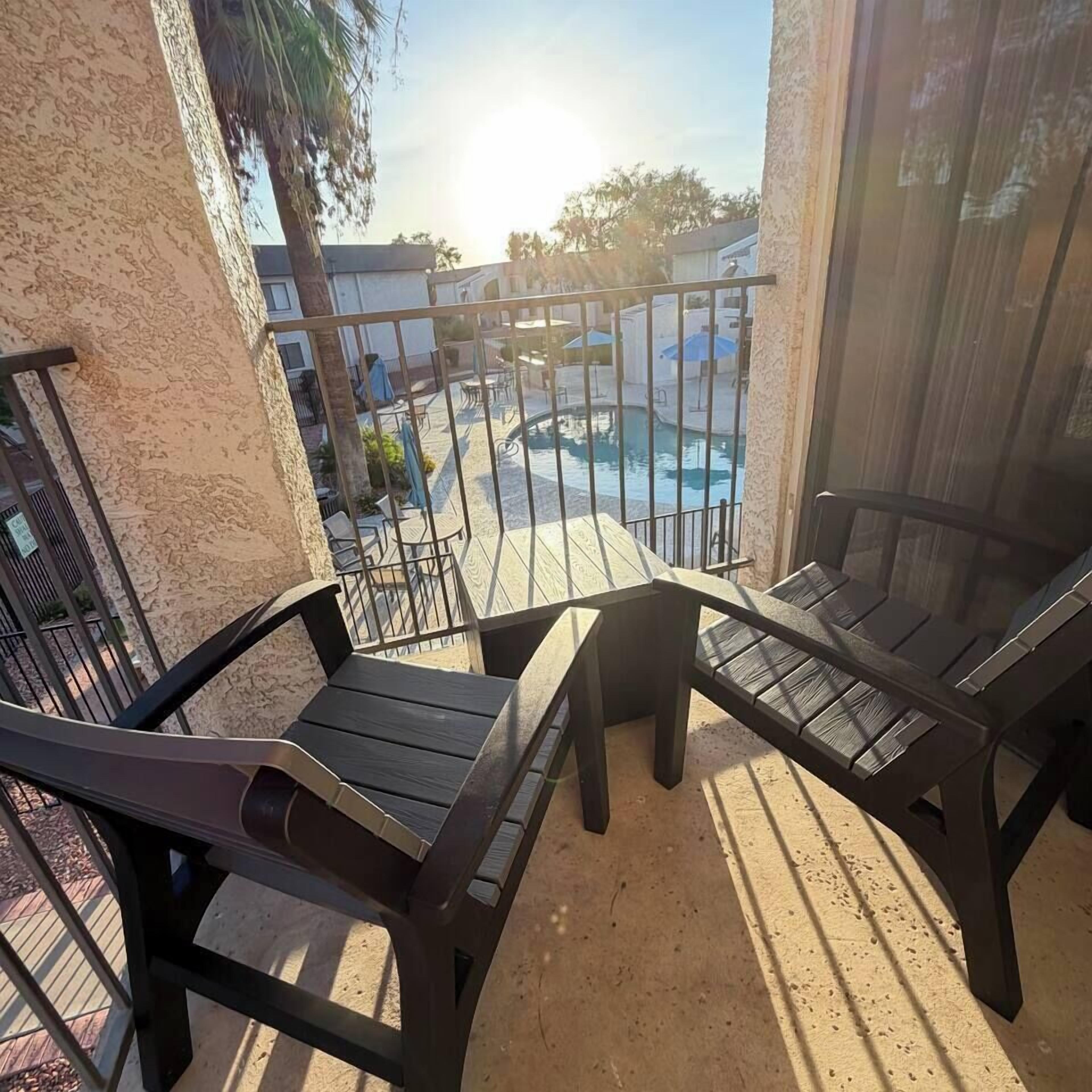 A balcony with two wooden chairs and a pool in the background.