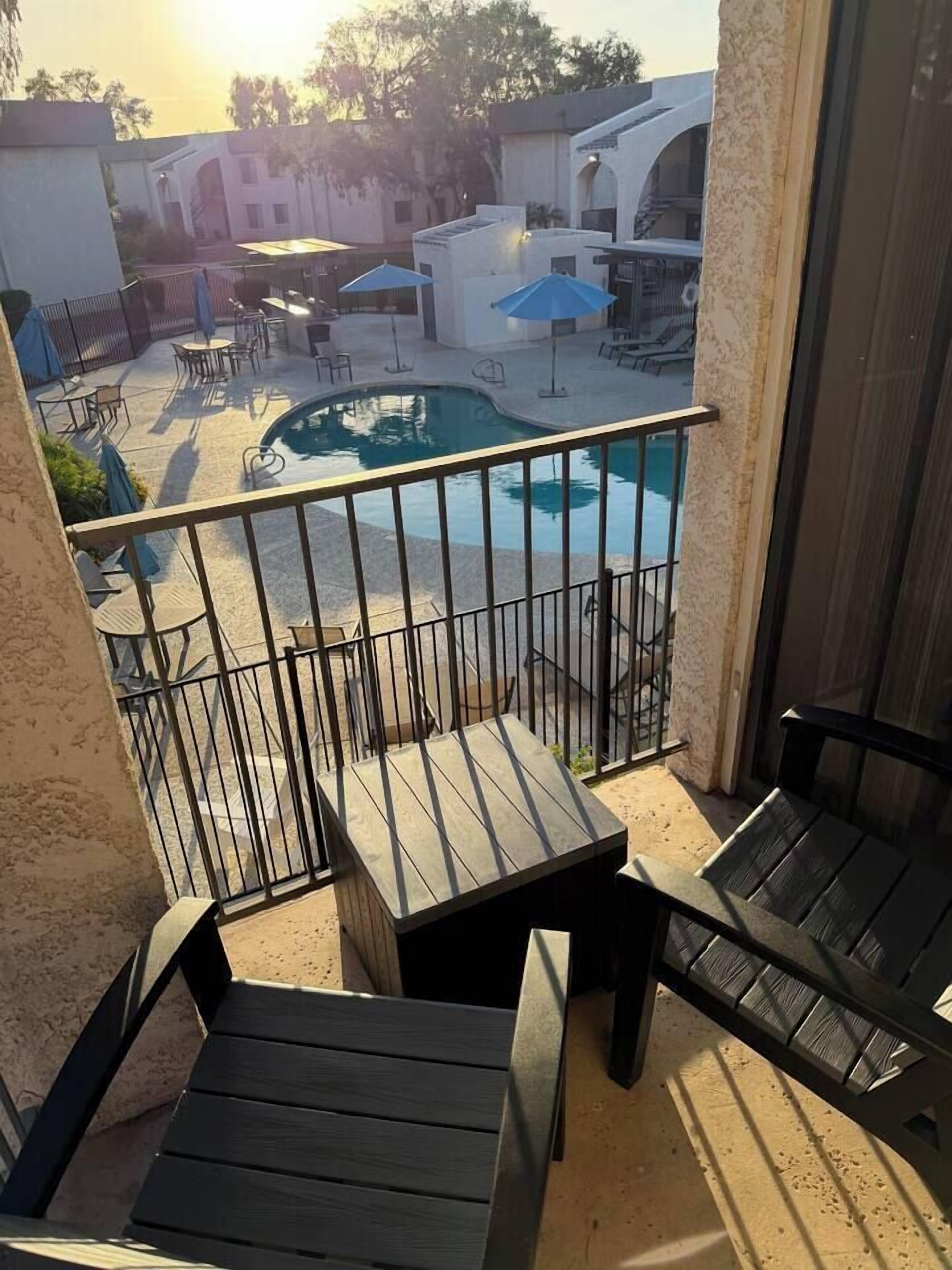 A balcony with a view of a swimming pool, outdoor furniture, and a building in the background.