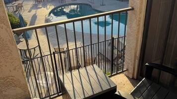 A balcony with a view of a swimming pool, outdoor furniture, and a building in the background.