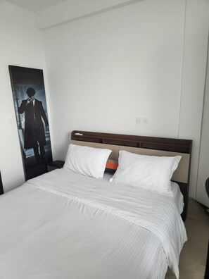 A hotel room with a large bed, white bedding, a wooden headboard, and a poster of a man in a suit on the wall. - Lumina T3 Pool and Gym (Abidjan)