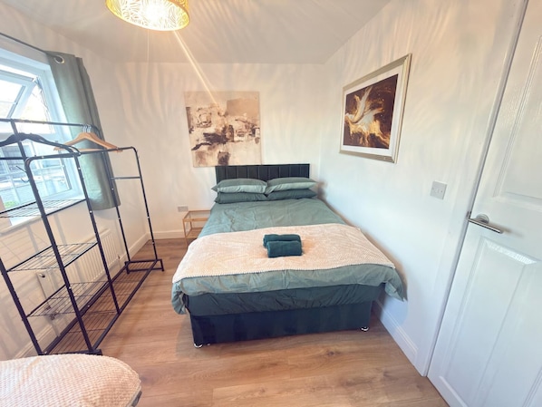 A bedroom with a bunk bed, a hanging clothes rack, a painting, and a door.
