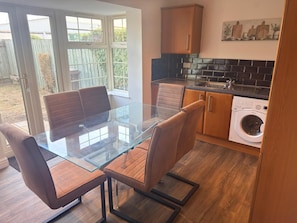 Une cuisine moderne avec une table à manger en verre, des chaises en cuir, un lave-linge encastré et un mur de fond en briques.