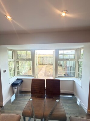 A room with a bay window, two cushioned chairs, a small table, and a trash bin.