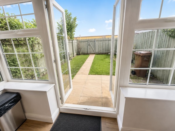 A view through a glass door into a backyard with a lawn and a wooden fence.