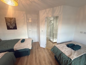 A hotel room with two beds, a shower, and a door leading to a bathroom.