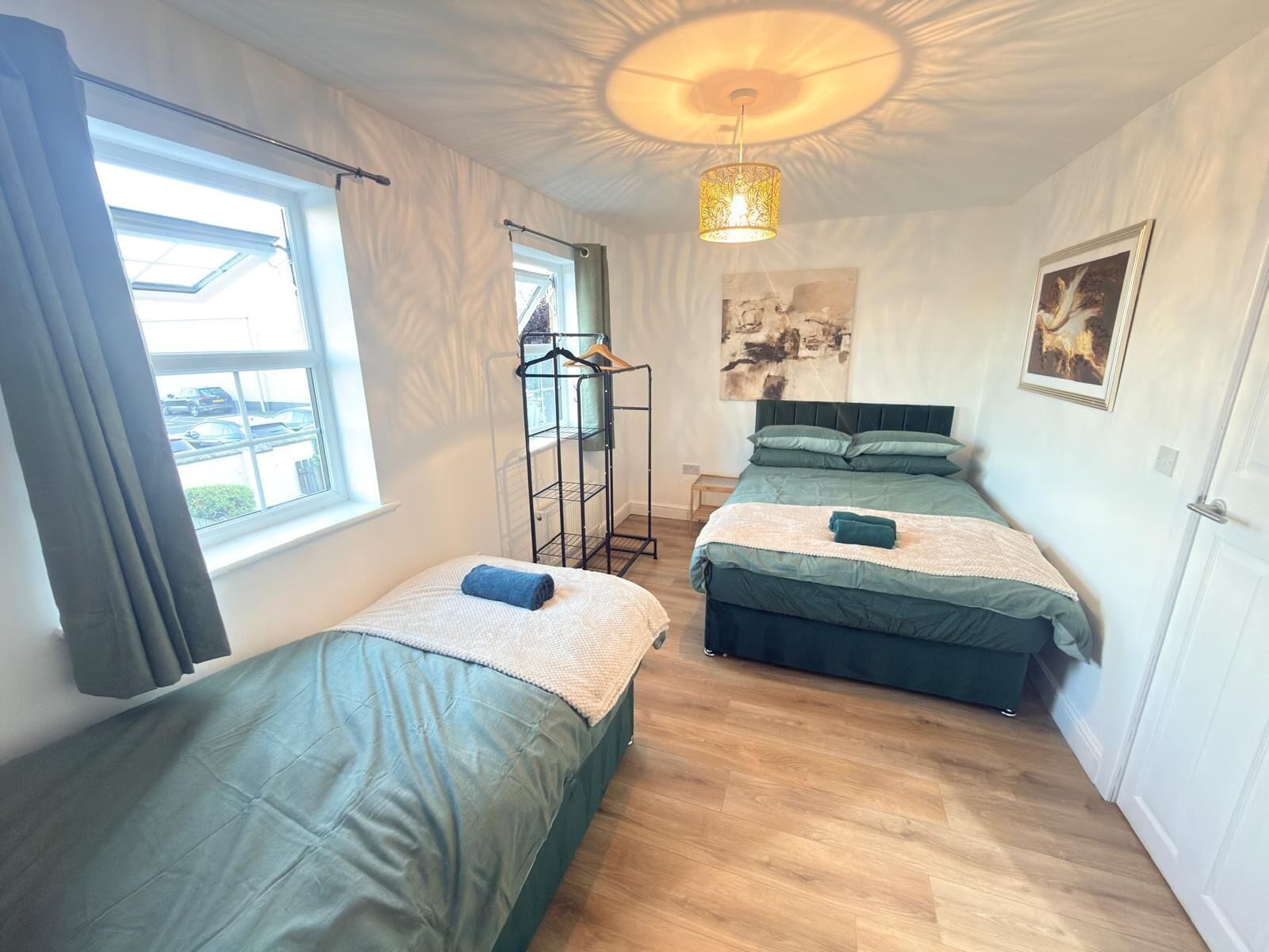 A room with two beds, a hanging light fixture, and a window with curtains.