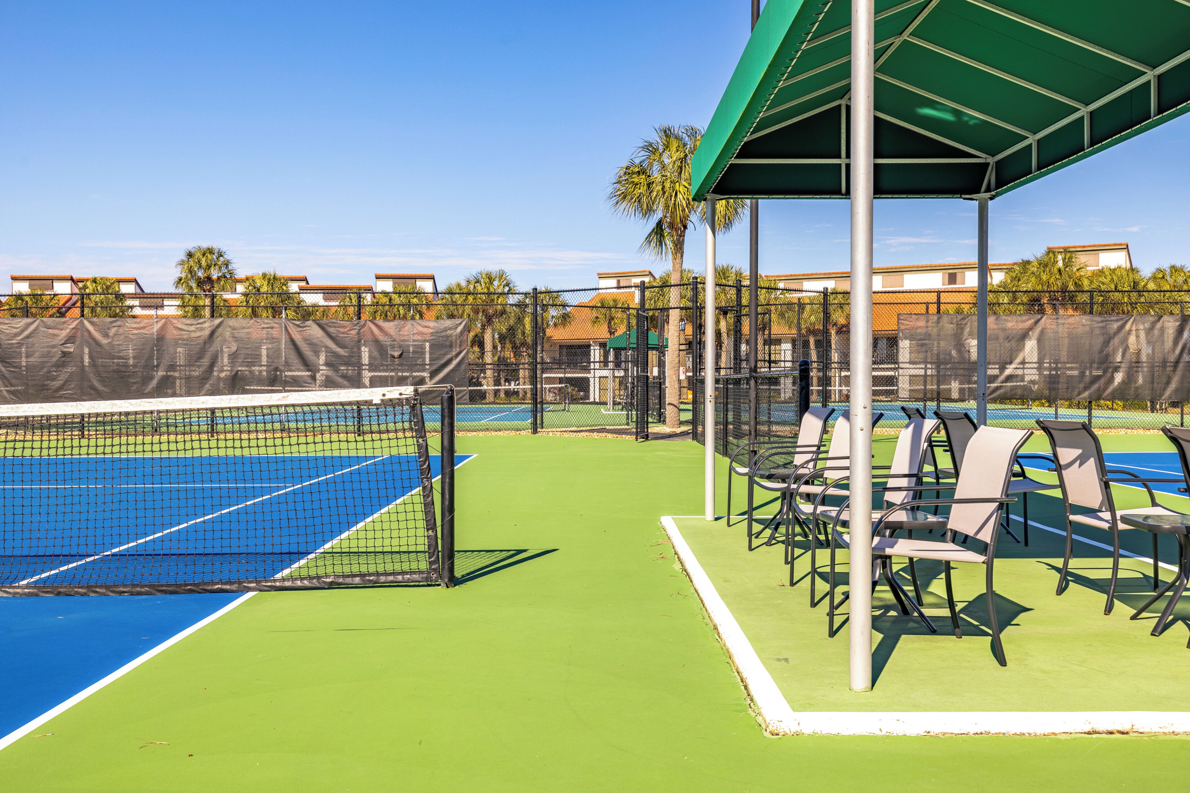 A tennis court with a green roofed seating area and chairs.