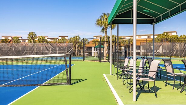 Een tennisbaan met een zitgedeelte met een groen dak en stoelen.