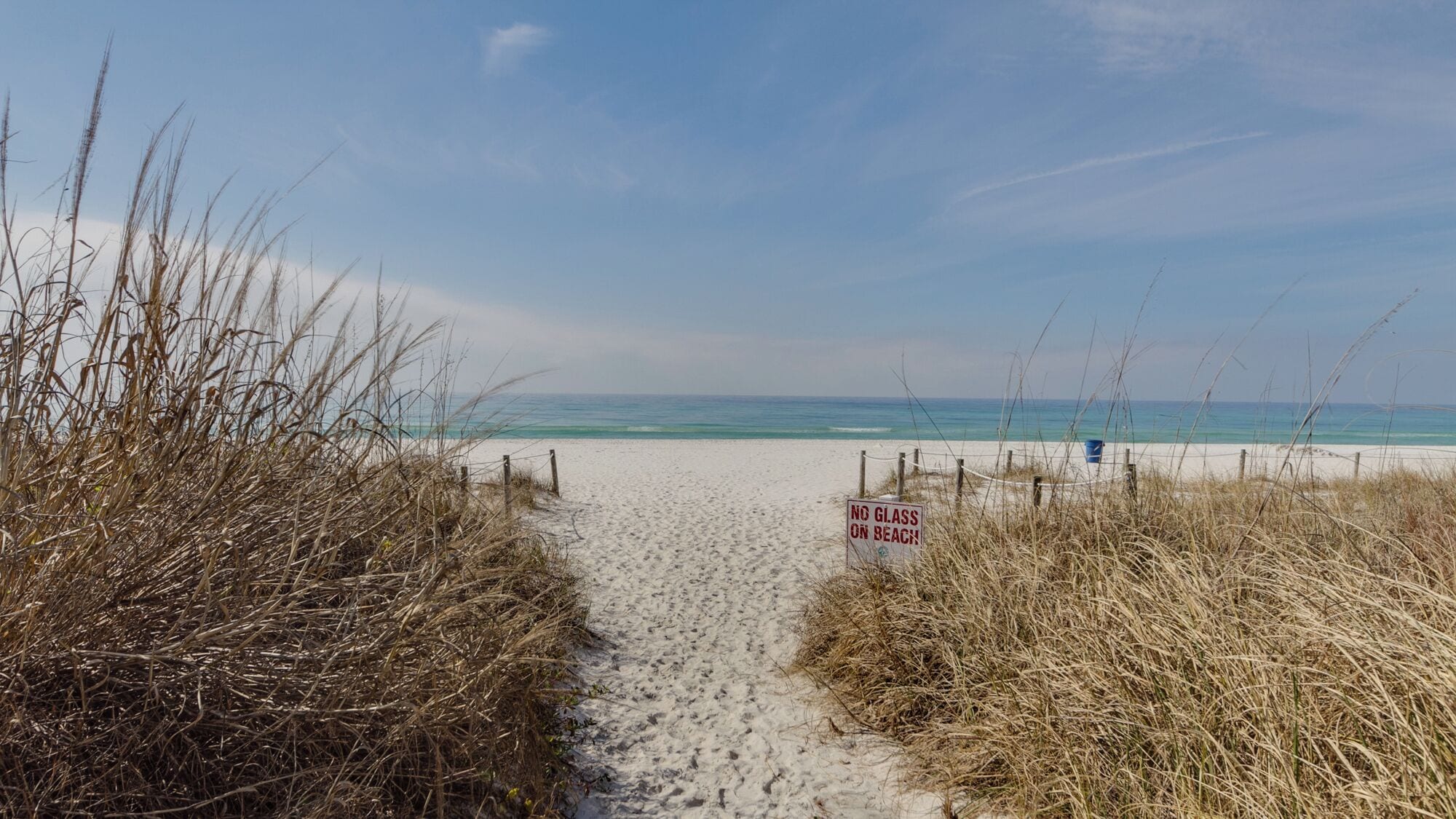 Ein Strandweg, der zum Meer führt, mit einem Schild, das 'No Glass on Beach' zeigt.
