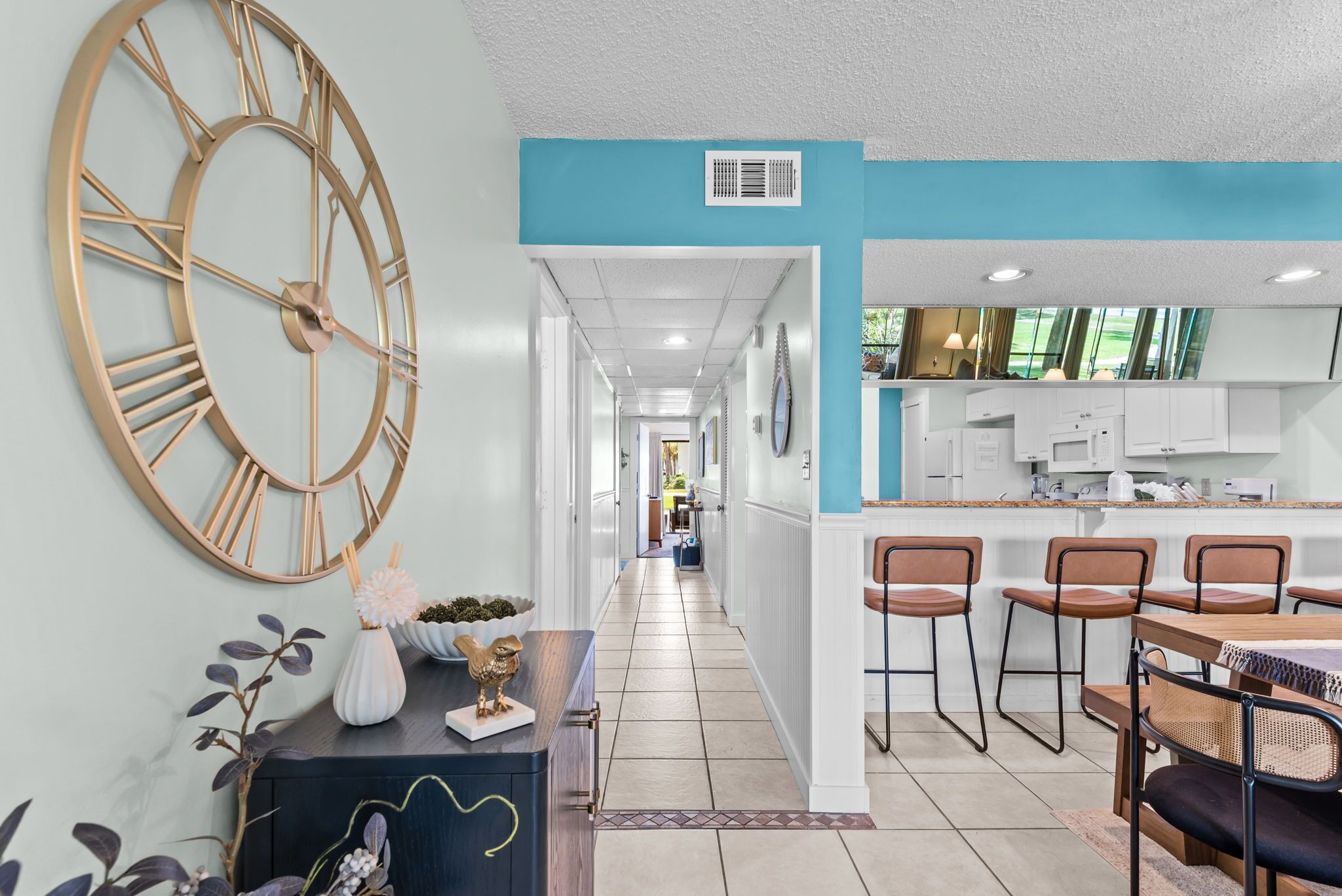 A modern kitchen with white cabinets, a large clock, and a dining area with bar stools.