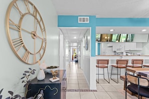 A modern kitchen with white cabinets, a large clock, and a dining area with bar stools. - 3BR Edgewater Condo Pools, Golf, Tennis & Private Beach Access! (Panama City Beach)