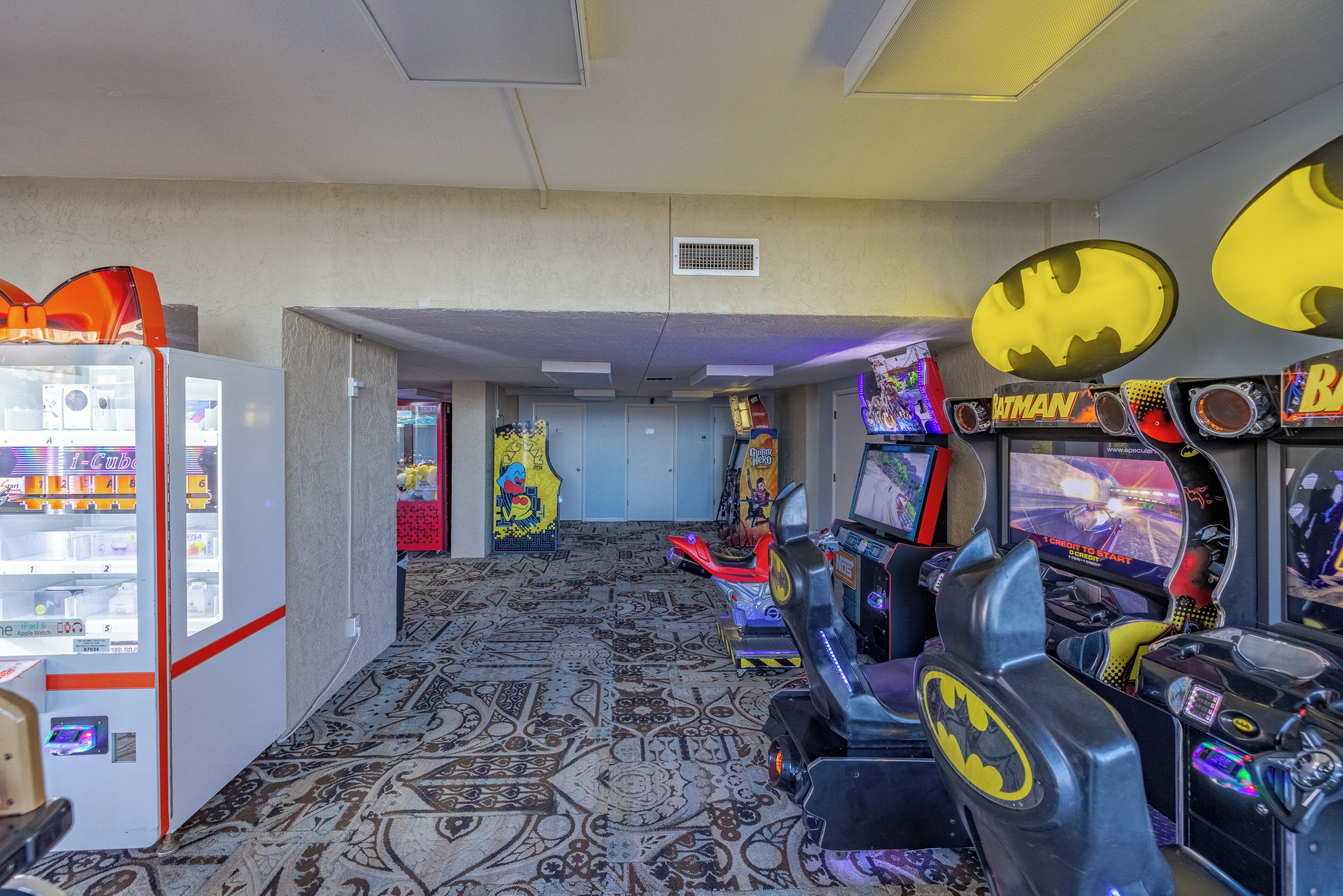 A gaming arcade with various Batman-themed machines and a vending machine.