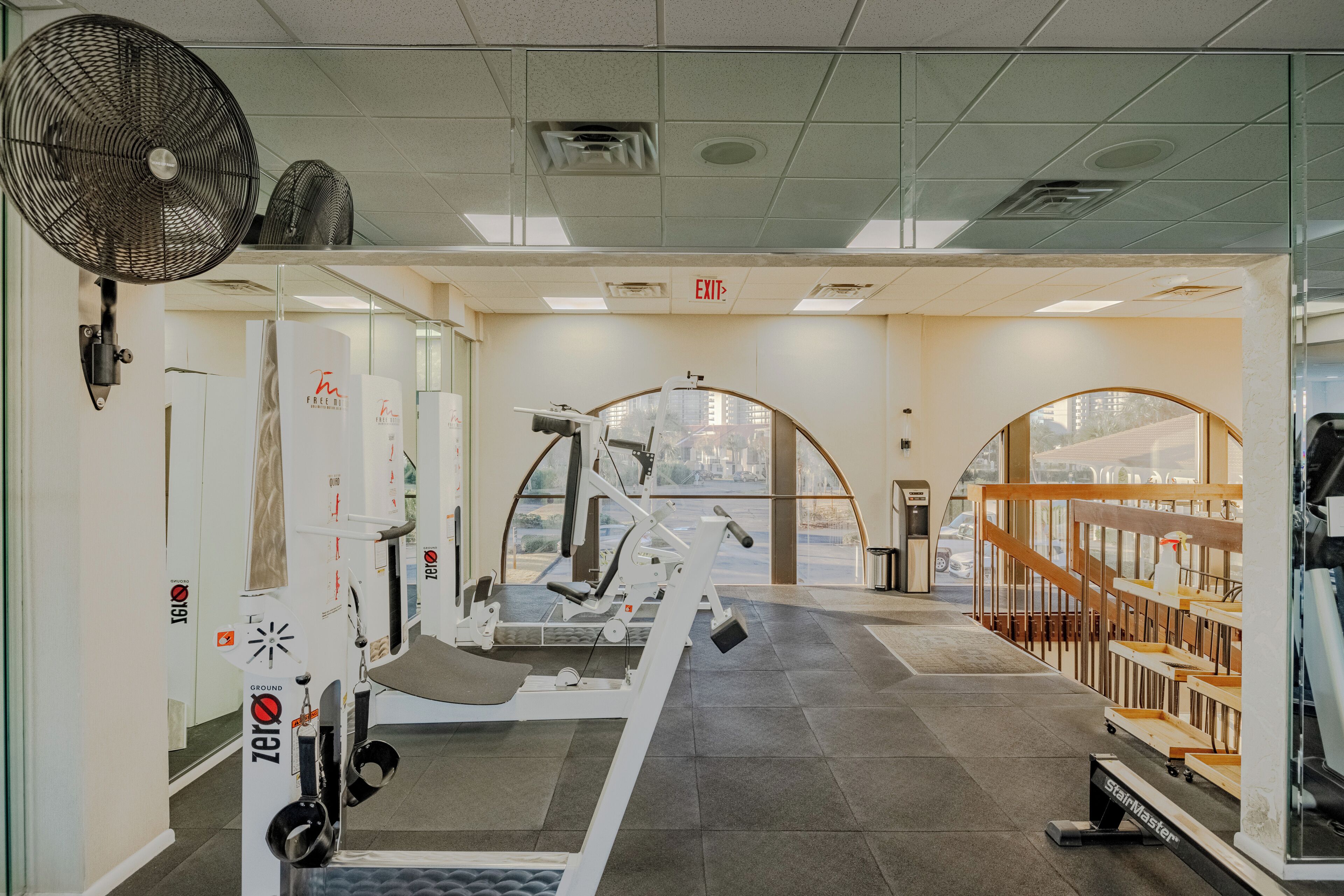 A gym with exercise equipment, a fan, and a view of the city through large windows.