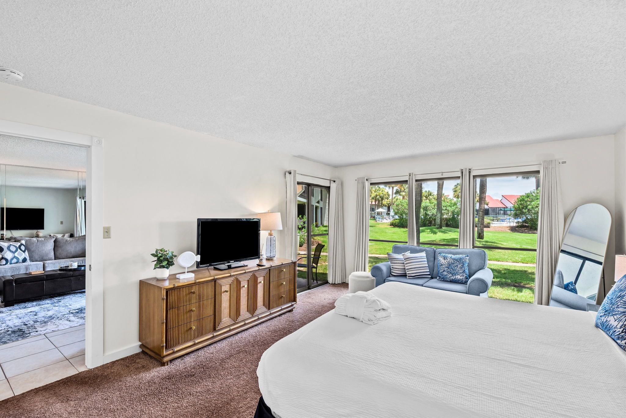 Un dormitorio con una cama grande, televisión, cómoda de madera y vistas a un jardín.