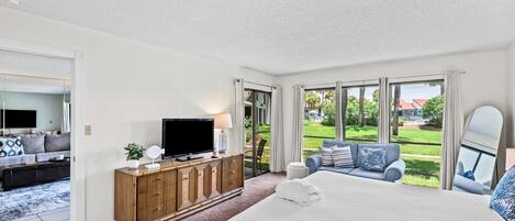 Un dormitorio con una cama grande, televisión, cómoda de madera y vistas a un jardín.