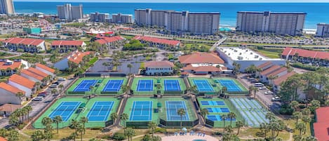 Un resort con múltiples canchas de tenis, piscina y vistas a la playa.