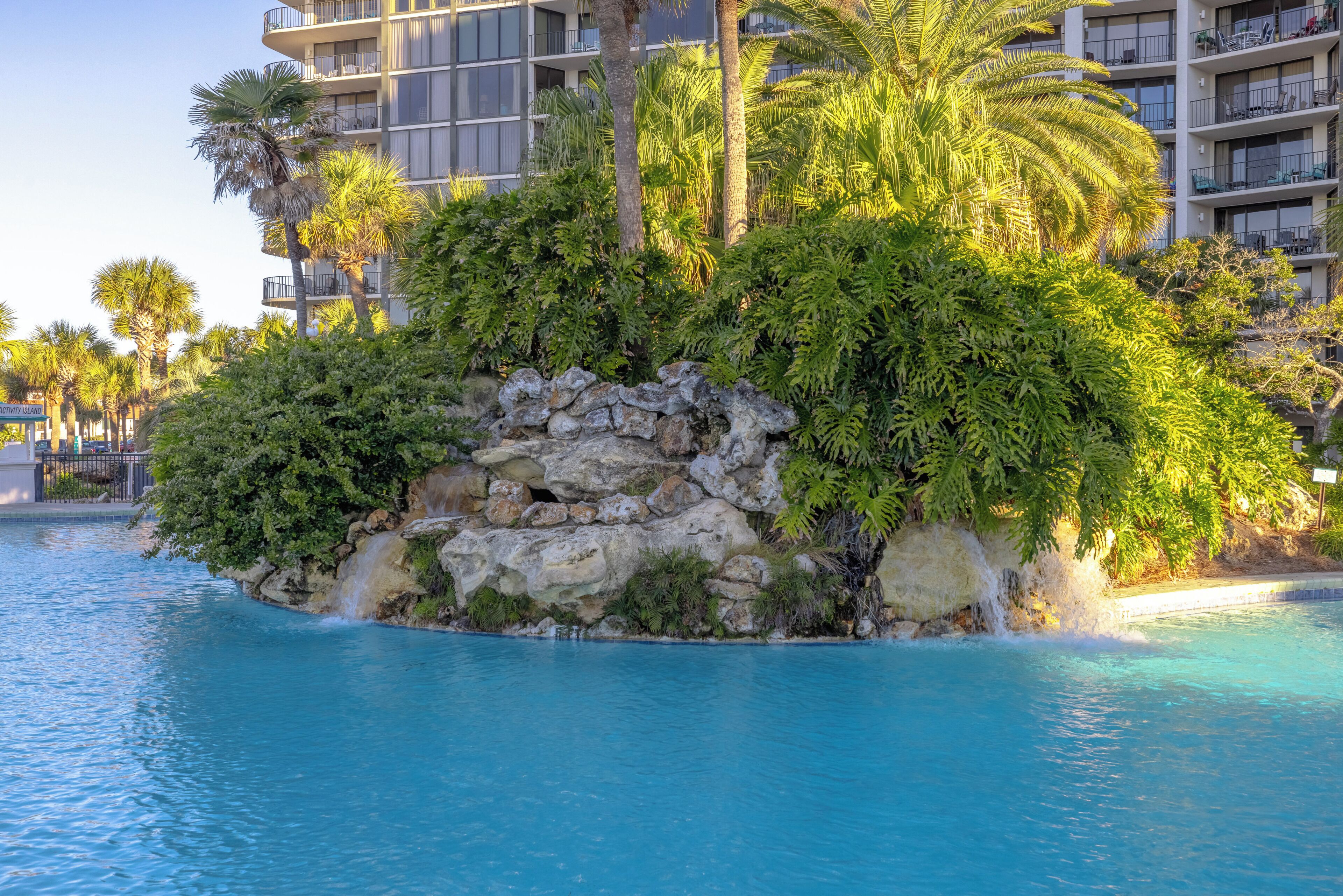 Une piscine entourée d’une végétation luxuriante et d’un îlot rocheux.