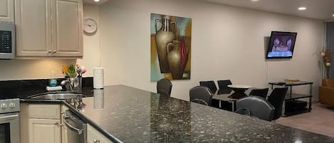 A modern kitchen with a granite countertop, stainless steel appliances, and a dining area with a table and chairs.