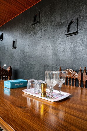 En bardisk med en mörk, strukturerad vägg, ett träpanelat tak och ett bord med glas och en låda märkt med texten ”Polyclay”.