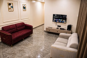 Ett vardagsrum med en röd soffa, en beige soffa, en tv som är monterad på väggen och ett avlastningsbord med elektronisk utrustning.