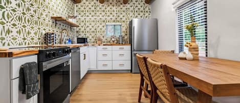 A modern kitchen with a wooden table and chairs, a refrigerator, and a patterned backsplash.