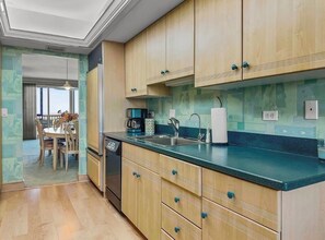 A kitchen with wooden cabinets, a black countertop, and a dining area with a table and chairs. - Spacious 3-bedroom condo with amazing Beach front views of the Gulf! (Sarasota)