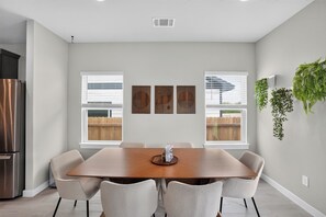 A modern dining room with a large wooden table, six chairs, and a refrigerator on the left. - Extended Stay - Private Gym - EV Charger - Workspace (Austin)