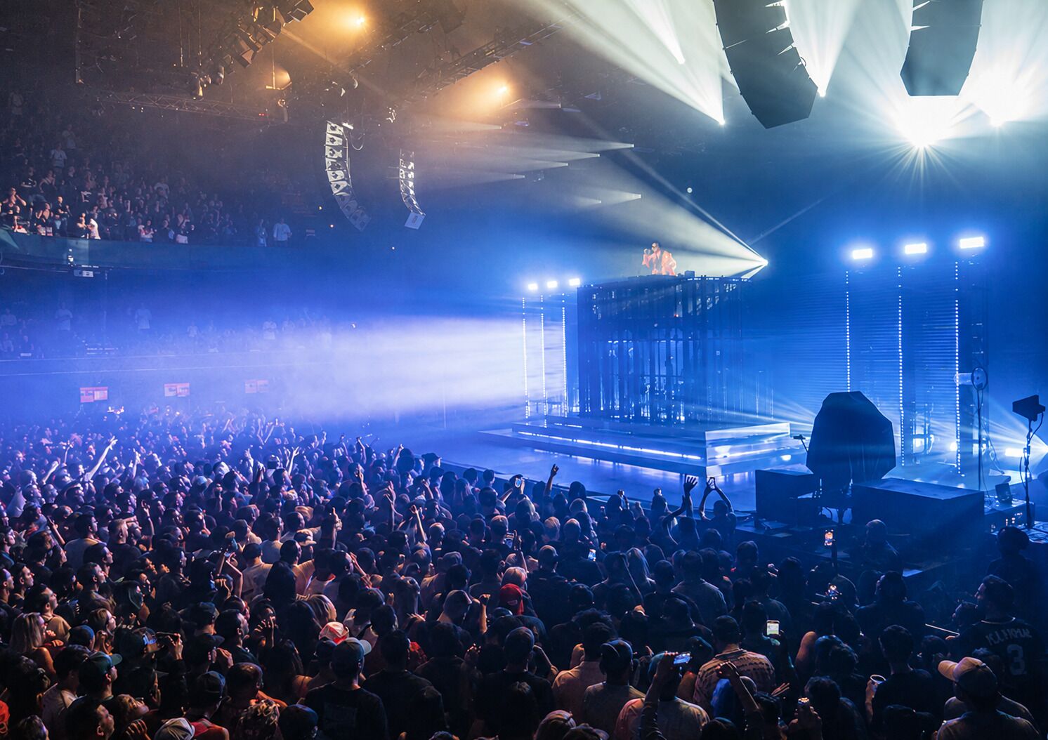 A crowded concert venue with a stage, lighting, and audience.