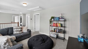 A modern living room with a sectional sofa, a black bean bag, a bookshelf, and a TV stand.