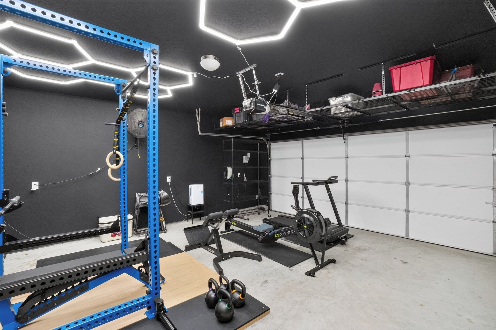Un gimnasio en casa con un rack de levantamiento de pesas azul, una bicicleta estática y una caminadora.