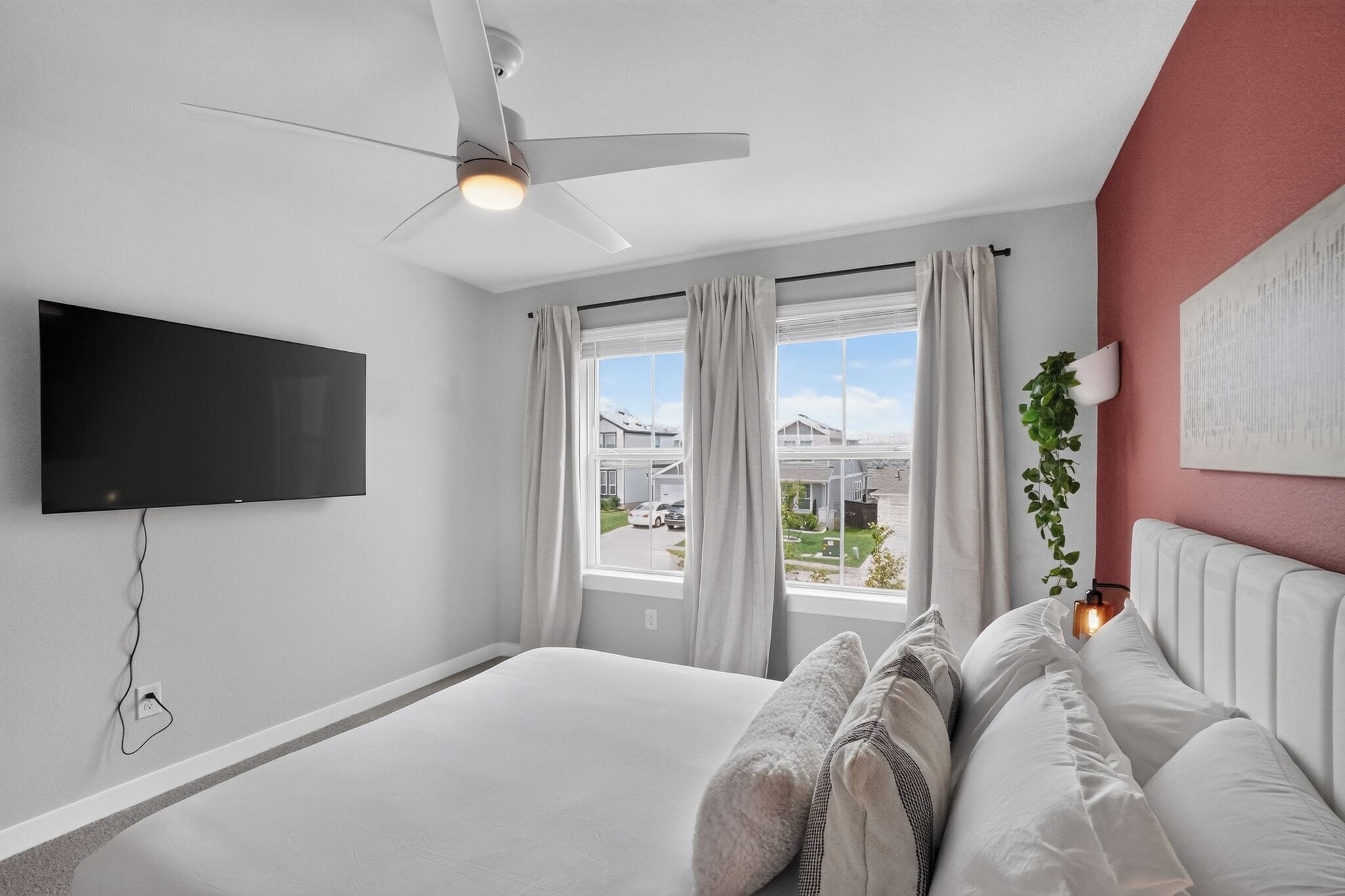 A bedroom with a bed, a ceiling fan, a TV, and a window with curtains.