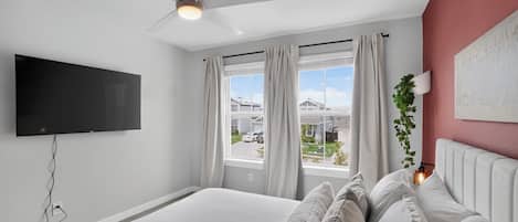 A bedroom with a bed, a ceiling fan, a TV, and a window with curtains.